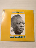 A vinyl record album cover for John Lee Hooker's 'That's Where It's At!' resting on a light-colored wooden surface. The cover features a bright yellow background with a central black and white portrait of the artist and bold black text outlined in teal.